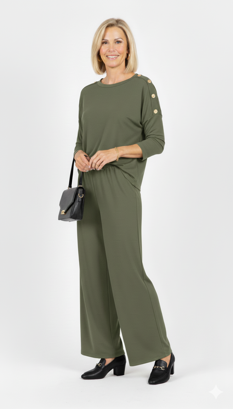 Vrouw draagt groene dames set met gouden knopen op de schouders en rechte broek  elegante co-ord outfit met zwarte tas en hakken.