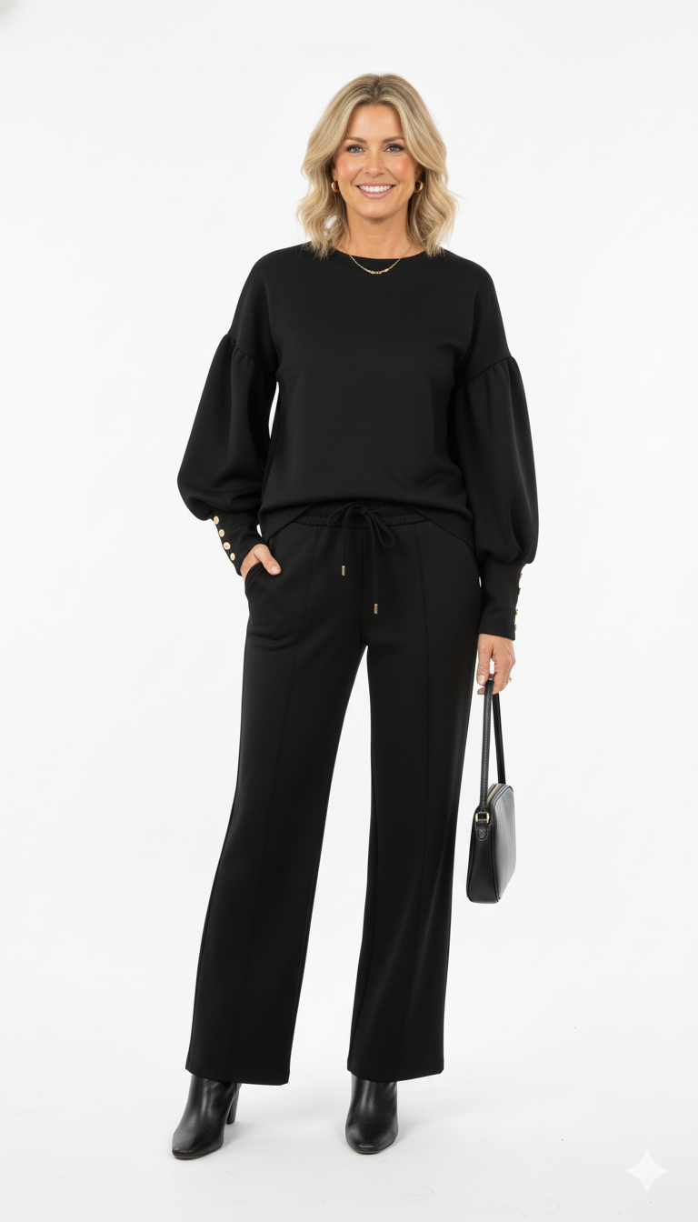 Vrouw draagt zwarte dames set met wijde mouwen en rechte broek elegante co-ord outfit met gouden details, zwarte enkellaarsjes en handtas.