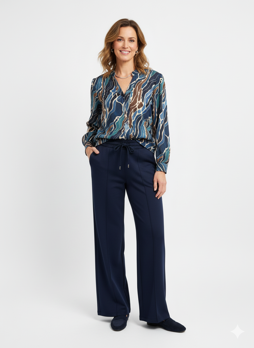 Model draagt een grafische damesblouse in blauw- en bruintinten met donkerblauwe broek.”

“Elegante damesoutfit met printblouse en donkerblauwe broek met elastische taille.”

“Stijlvolle grafische blouse gecombineerd met donkerblauwe damesbroek.”

“Comfortabele en chique damesoutfit met blouse met print en rechte broek.”

“Moderne dameslook: grafische blouse en donkerblauwe broek.”