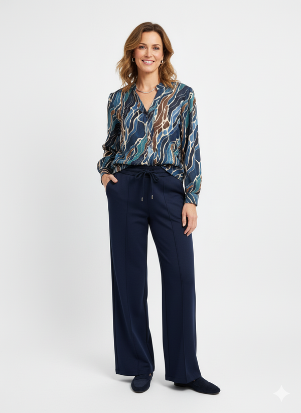 Model draagt een grafische damesblouse in blauw- en bruintinten met donkerblauwe broek.”

“Elegante damesoutfit met printblouse en donkerblauwe broek met elastische taille.”

“Stijlvolle grafische blouse gecombineerd met donkerblauwe damesbroek.”

“Comfortabele en chique damesoutfit met blouse met print en rechte broek.”

“Moderne dameslook: grafische blouse en donkerblauwe broek.”
