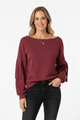 Vrouw met bordeauxrode top met geplooide mouwen, gecombineerd met zwarte broek – elegante damesblouse voor een moderne en stijlvolle look.