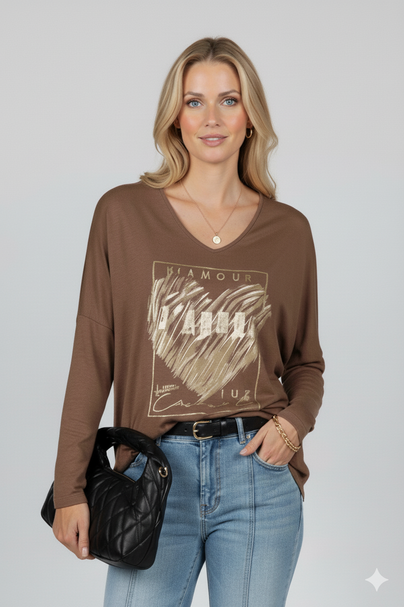 Vrouw met bruine V-hals top met gouden “L’Amour J’Adore” hartprint, gecombineerd met jeans en gouden sieraden – modieuze damesblouse voor een chique casual look.