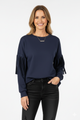 Vrouw met donkerblauwe top met geplooide mouwen, gecombineerd met zwarte broek – elegante damesblouse met stijlvolle details voor een moderne look.