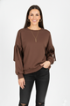 Vrouw met bruine top met geplooide mouwen, gecombineerd met zwarte broek – stijlvolle damesblouse met unieke mouwdetails en moderne uitstraling.