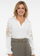 Witte damesblouse met geborduurde bloemdetails op de mouwen.