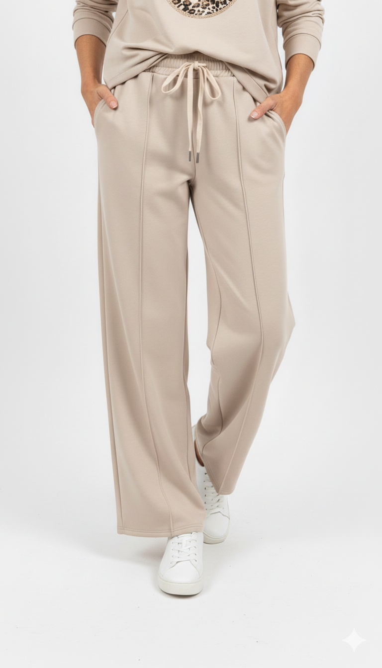 Vrouw draagt beige wide leg broek met strikceintuur en witte sneakers – stijlvolle en comfortabele look.