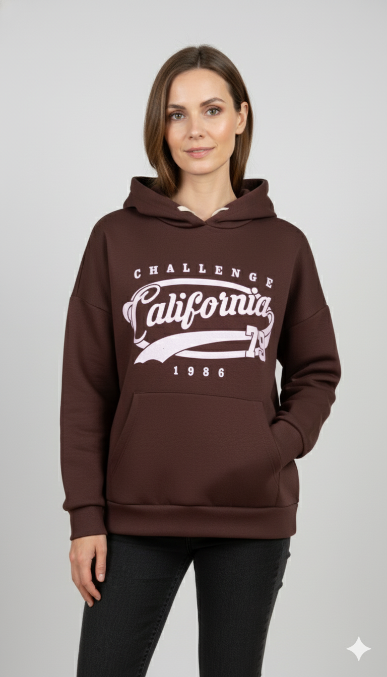 Vrouw met bruine hoodie met ‘California Challenge 1986’ print en capuchon – casual damestrui met sportieve vintage uitstraling.