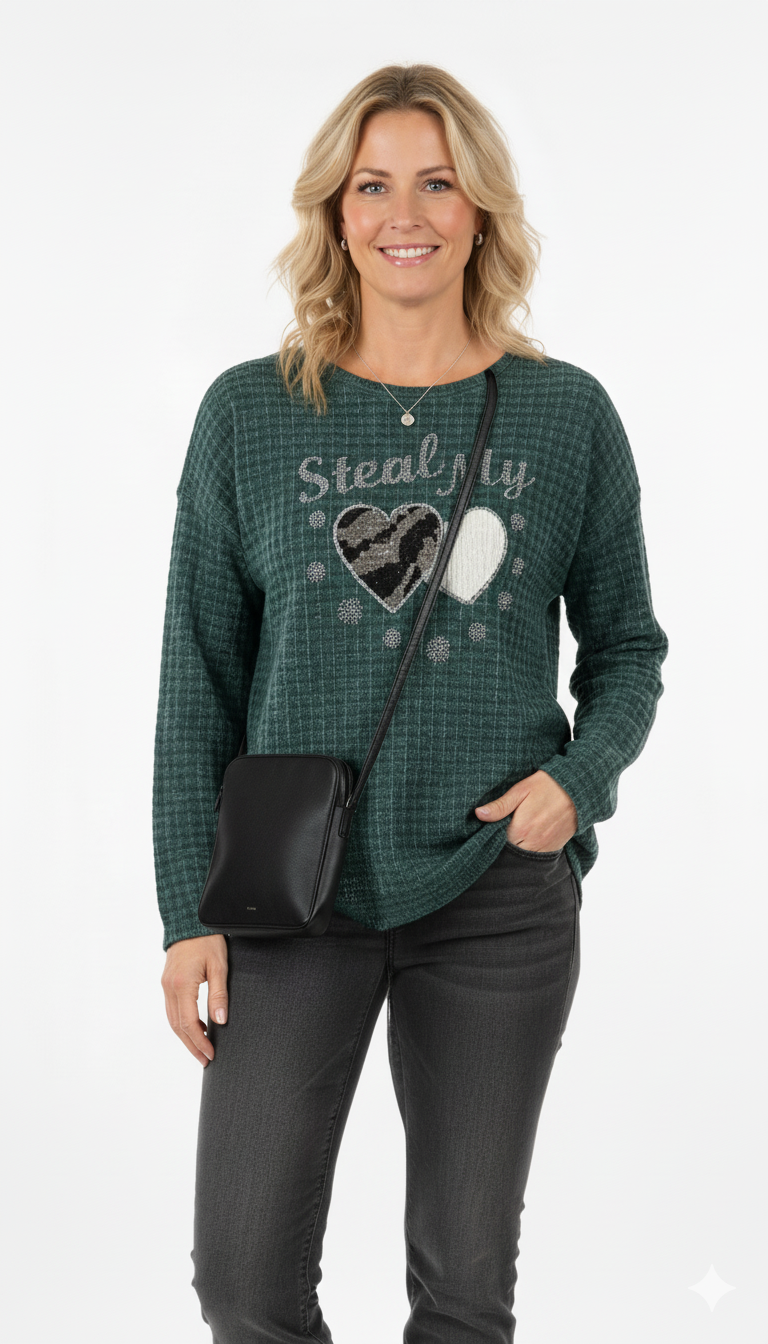 Vrouw draagt groene trui met ‘Steal My Heart’-print en hartjes, gecombineerd met zwarte jeans en schoudertas – casual-chique look.