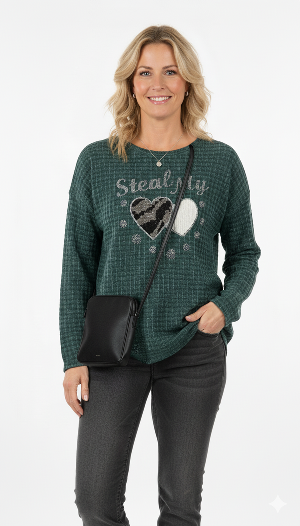 Vrouw draagt groene trui met ‘Steal My Heart’-print en hartjes, gecombineerd met zwarte jeans en schoudertas – casual-chique look.
