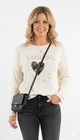 Vrouw draagt beige trui met glinsterende ‘Steal My Heart’-print en hartjes, gecombineerd met zwarte jeans en tas.