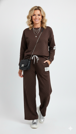 Vrouw draagt bruin joggingpak met witte stippen – comfortabele dames loungewear set met rechte broek en trekkoord.