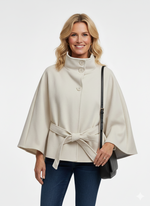 Vrouw draagt crèmekleurige cape met strikceintuur en knoopsluiting – elegante damesjas met hoge kraag.