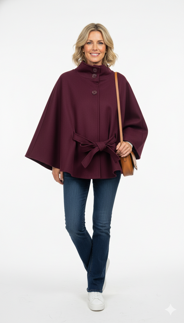 Vrouw draagt bordeauxrode cape met strikceintuur en knoopsluiting – elegante herfstjas met luxe uitstraling.