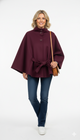 Vrouw draagt bordeauxrode cape met strikceintuur en knoopsluiting – elegante herfstjas met luxe uitstraling.