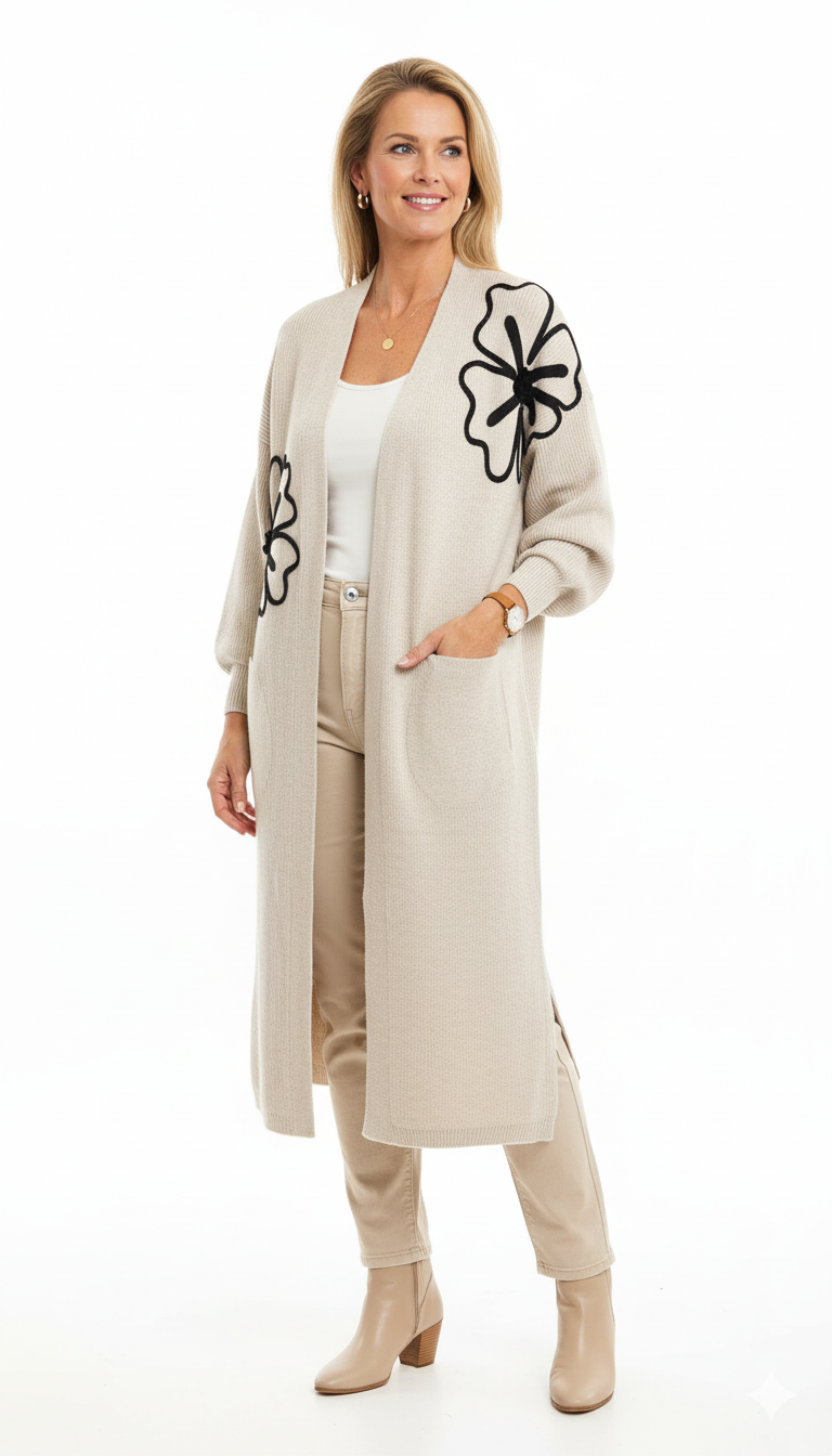 Model draagt een beige lang vest met zwarte bloemenapplicatie van Blushfashionstore, gecombineerd met een witte top en beige broek.