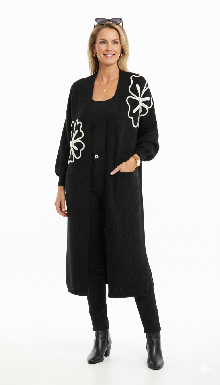 Model draagt een zwart lang vest met witte bloemenapplicatie van Blushfashionstore, gecombineerd met een zwarte top en broek.