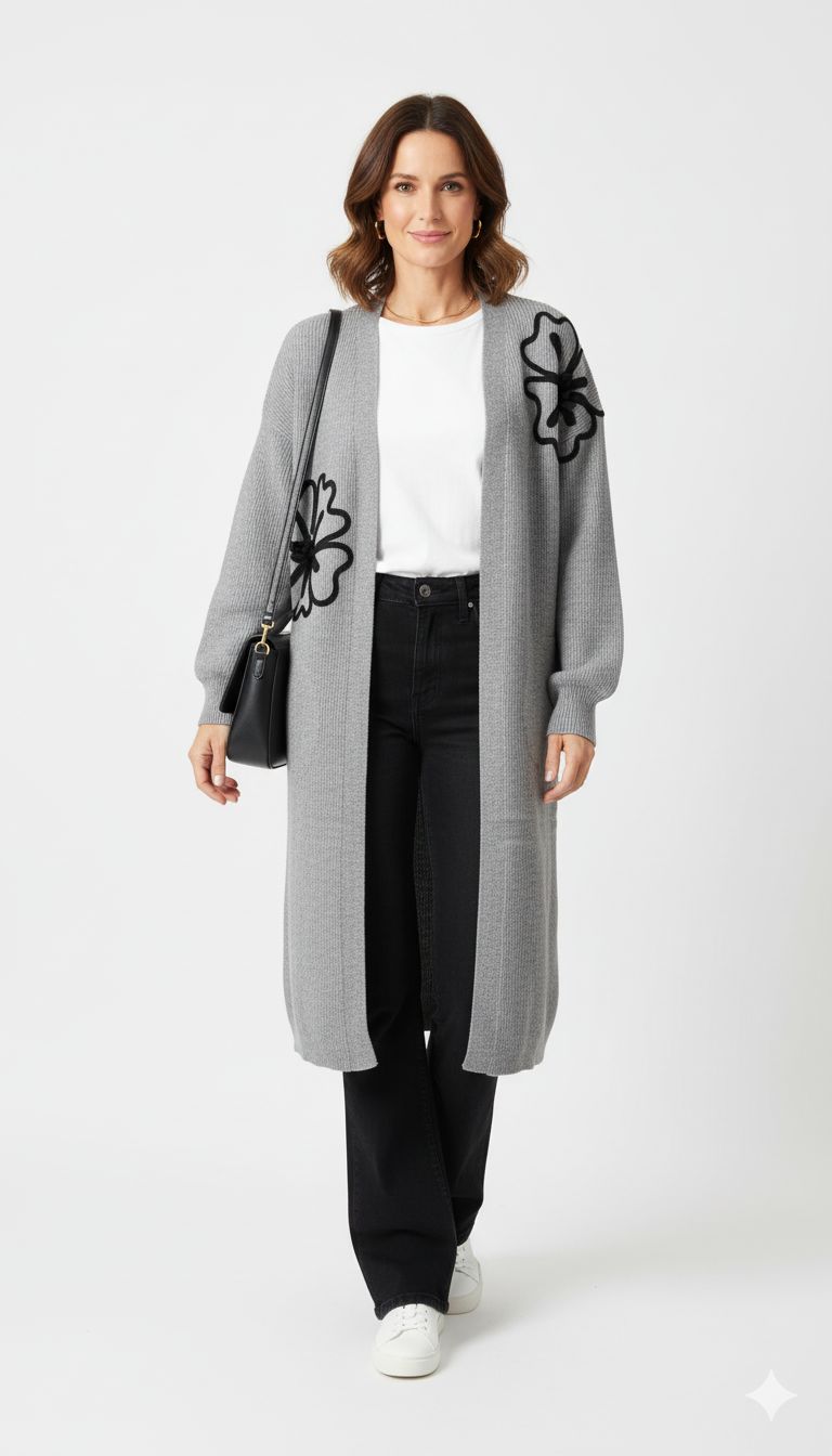 Model draagt een lang grijs vest met zwarte bloemenapplicatie van Blushfashionstore, gecombineerd met een witte top en zwarte broek.