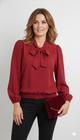 Model draagt een rode glitterblouse met strik van Blushfashionstore, gecombineerd met een zwarte broek en een rode velvet clutch.